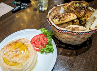 Traditional hummus topped with olive oil, served with a basket of fresh bread on a table at a local restaurant in Riyadh, Saudi Arabia
