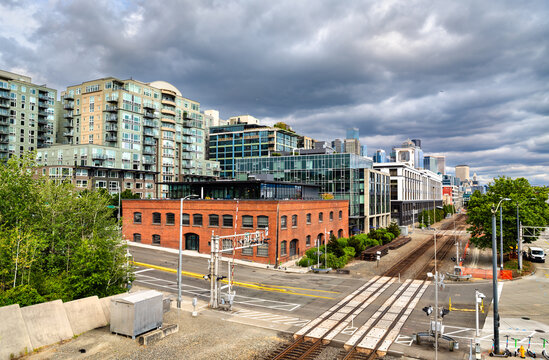 A mix of modern residential and historic brick buildings along railroad tracks in Seattle, Washington, USA. The urban cityscape is seen under a dramatic cloudy sky