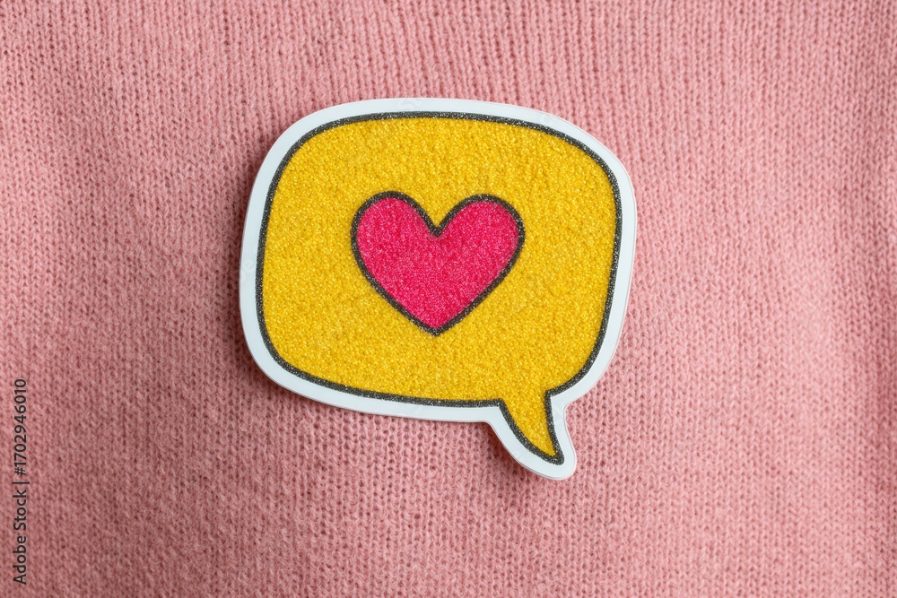 Poster a colorful speech bubble with a heart symbol softly resting on a cozy pink fabric expressing emotion