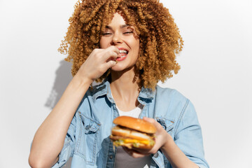 Cheerful young woman enjoying a delicious hamburger against a light background, embodying healthy...