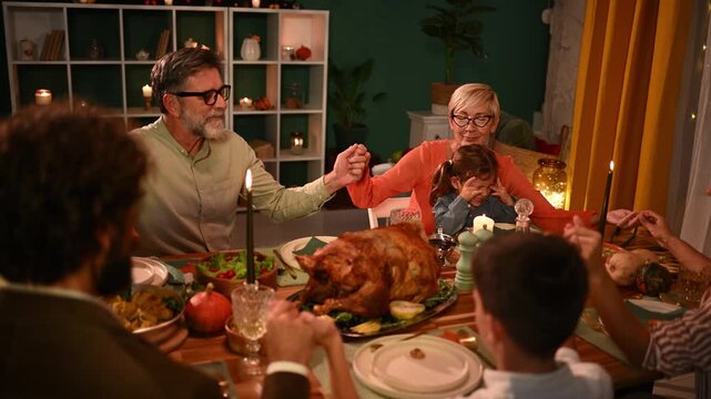 Family holding hands, praying before thanksgiving dinner