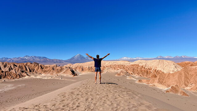 Unrecognisable tourist man standing on the top of dune with raised arms above head, looking at spectacular Licancabur volcano in Death Valley, close to San Pedro de Atacama in Chile. Tourist sand dune