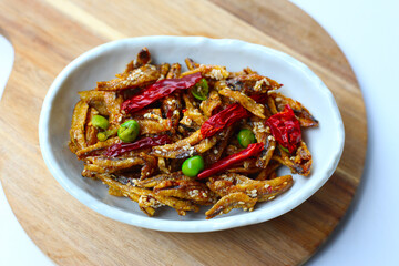 Crispy fried anchovies with sesame, dried chili, green peas, and herbs on white background.