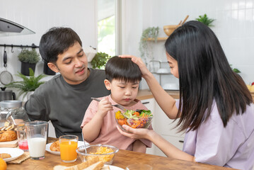 happy family together. Asian parent eating breakfast with little son in the kitchen.
