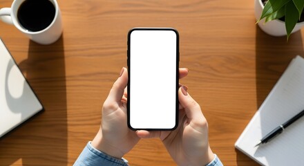 Hands holding a blank screen smartphone on a wooden desk, ideal for app mockups, digital content display, and showcasing modern technology