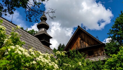 Wooden church steeple and buildings amidst greenery under a partly cloudy sky