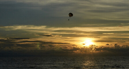 Parasailing at sunset over ocean with dramatic sky and clouds.