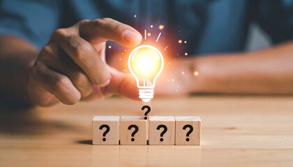 Hand holding lightbulb over question marks on wooden blocks