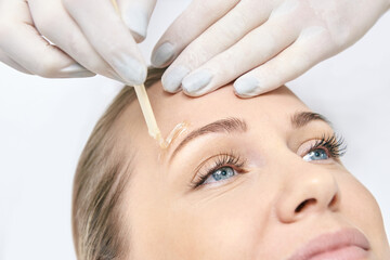 Caucasian female adult eyebrow waxing with applicator in salon setting close-up.
