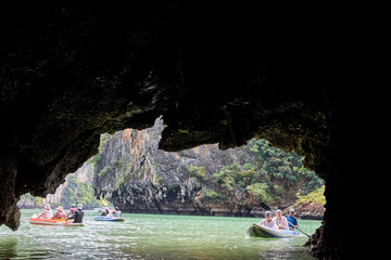 PHUKET, THAILAND - 12 NOVEMBER 2017: Tourists exploring scenic cave in kayaks on serene green lake surrounded by rocky cliffs and lush vegetation.