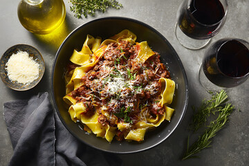 Black bowl of pappardelle pasta topped with rich meat sauce and freshly grated parmesan cheese, highlighting a delicious Italian dish.