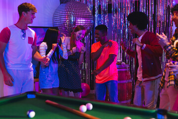 Teens dancing joyfully at party near pool table under disco ball lights
