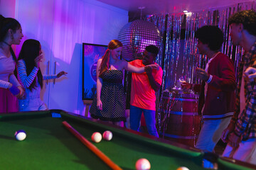 Teens celebrating at party, dancing near pool table under disco ball lights
