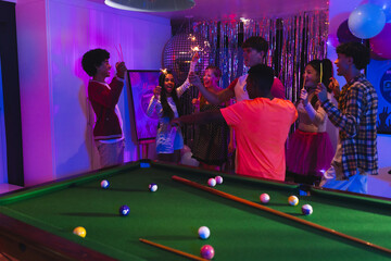 Teenagers celebrating around pool table with colorful lights and festive decorations