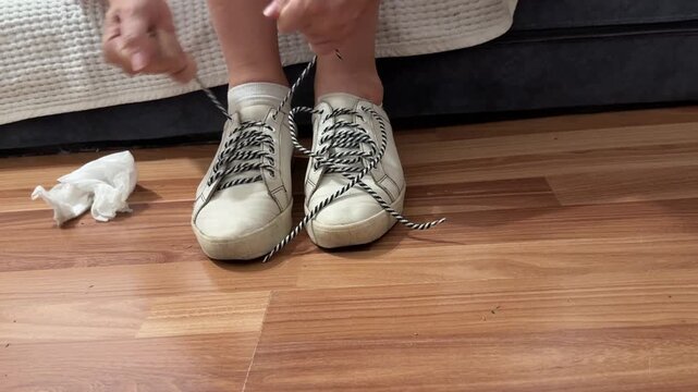 Close-up of a woman&rsquo;s hands tying shoelaces on worn white sneakers, unrecognizable. Lifestyle, daily routine, footwear