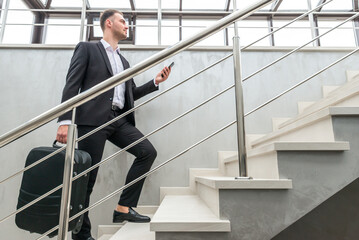 Businessman holding suitcase running on stairs in modern building