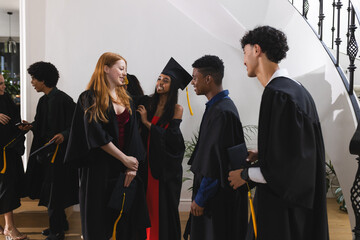 Teens in graduation gowns celebrating together, smiling and chatting indoors