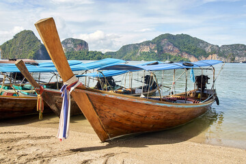 Traditional longtail boats on sandy beach with scenic mountain view in tropical thailand.