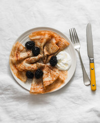 Crepes served with blackberries, yogurt and honey on a light background, top view