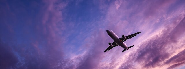 Modern passenger airplane flying high in colorful dramatic purple sky at sunset, concept of travel and transportation