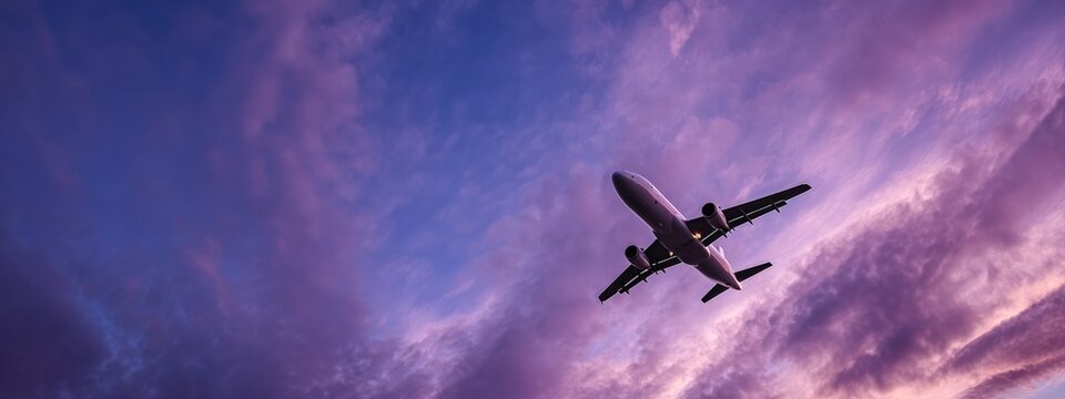 Fototapeta Modern passenger airplane flying high in colorful dramatic purple sky at sunset, concept of travel and transportation