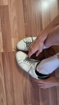 Close-up of a woman&rsquo;s hands unlacing worn white sneakers, shoelaces removed from eyelets. Footwear detail, casual routine, unrecognizable