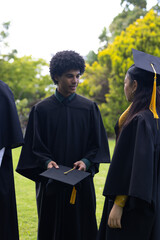 Graduates in caps and gowns celebrating outdoors, sharing joyful conversation