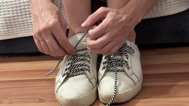 Close-up of a woman&rsquo;s hands unlacing worn white sneakers, shoelaces removed from eyelets. Footwear detail, casual routine, unrecognizable