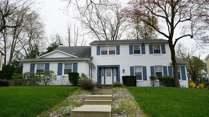 Front view of suburban white-painted brick house with blue shutters and landscaped lawn