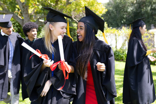 Graduating students outdoors in caps and gowns, holding diplomas and celebrating