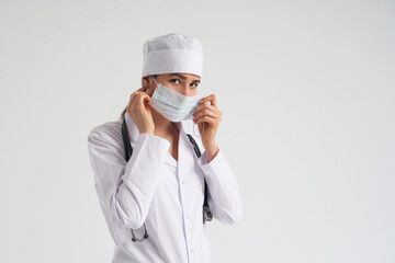 Portrait of young female doctor putting on protective medical face mask on white background, copy space