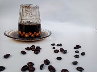 Freshly brewed black coffee served in an inverted cup with coffee beans spread around, representing...
