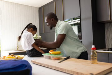 Father helping daughter with school uniform in kitchen, preparing for school