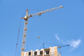 Tower cranes on construction site against clear blue sky with partial building view.
