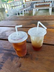 Sweet and fresh iced tea, in a plastic hood container, on a wooden table, menu in a cafe with open views of nature.