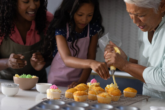 In kitchen, three generations decorating cupcakes, sharing family bonding time together