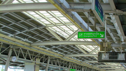 A modern station ceiling with glass panels and a green directional sign, captured in vintage tones with retro film grain.