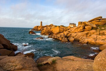 Scenic view of the Ploumanac'h lighthouse on the Pink Granite Coast in Brittany, France. Waves crash on the unique reddish rocks during golden hour. Famous travel destination in Europe.