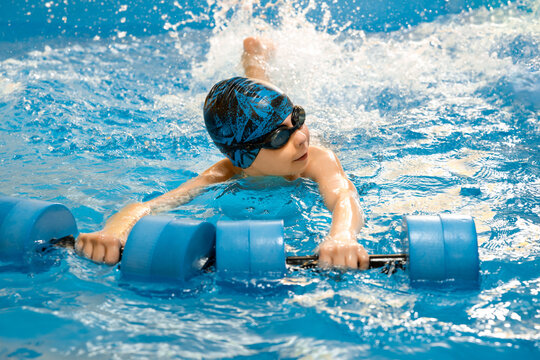 Boy swimming with water dumbbells in hands in swimming pool - Powered by Adobe