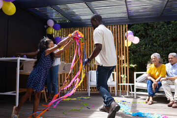 Celebrating outdoors, family dancing with colorful streamers, sharing joyful moments together