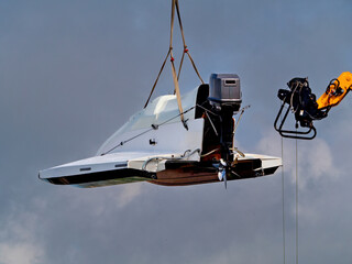 Motorboat with outboard engine lifted by crane against cloudy sky. Transportation and maintenance of marine equipment.