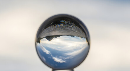 Transparent crystal sphere artfully reflects an inverted majestic landscape and expansive sky, showcasing a unique optical phenomenon