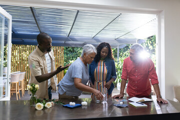 Family gathering at home, three generations preparing table with flowers and glasses