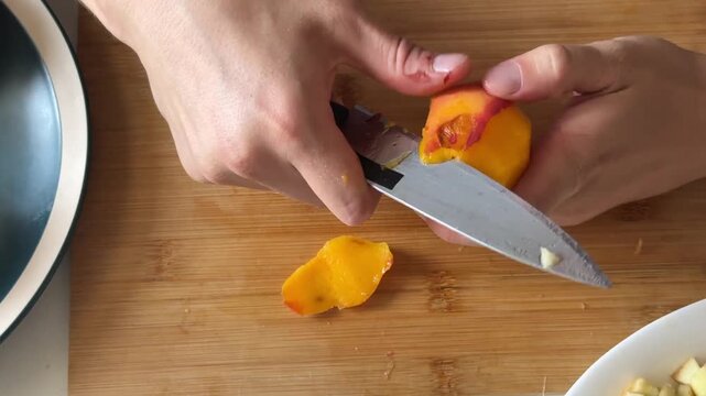 Man&rsquo;s hands peeling and cutting a peach close-up on a wooden board. Homemade fruit salad preparation, part of series. Unrecognizable