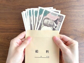 木製テーブルで給料袋に入ったお金を持つ女性の手元