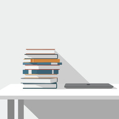 A stack of books and a laptop on a white desk against a plain wall.