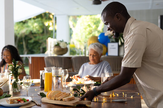 Serving fresh bread at family gathering, smiling and enjoying outdoor meal together - Powered by Adobe