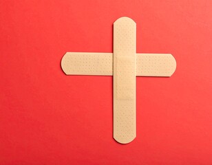 Adhesive bandages crossed to form a plus sign on a red surface