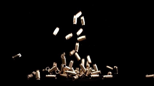 Slow motion footage of empty bullet shells falling against a black background, dramatic cinematic impact with metallic reflections, ammunition motion detail, dark atmosphere, and intense visual symbol