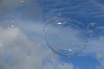 Soap bubble against a blue sky with few clouds and trees
